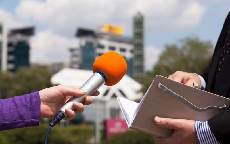 A man holding a microphone and a paper, symbolizing mass media and communication.