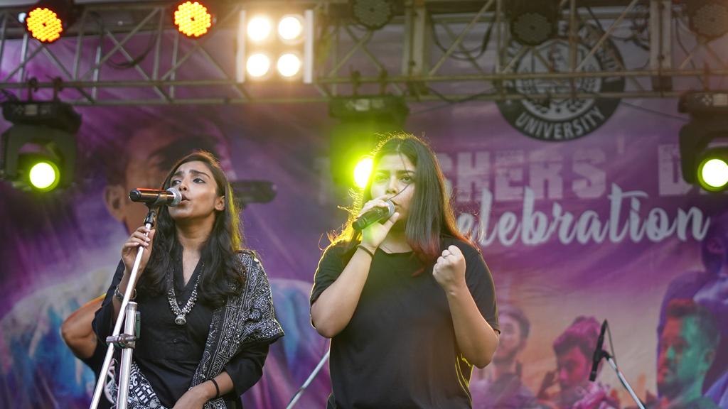 Two vocalists sharing the mic stand in front of the Freshers' Day Celebration backdrop