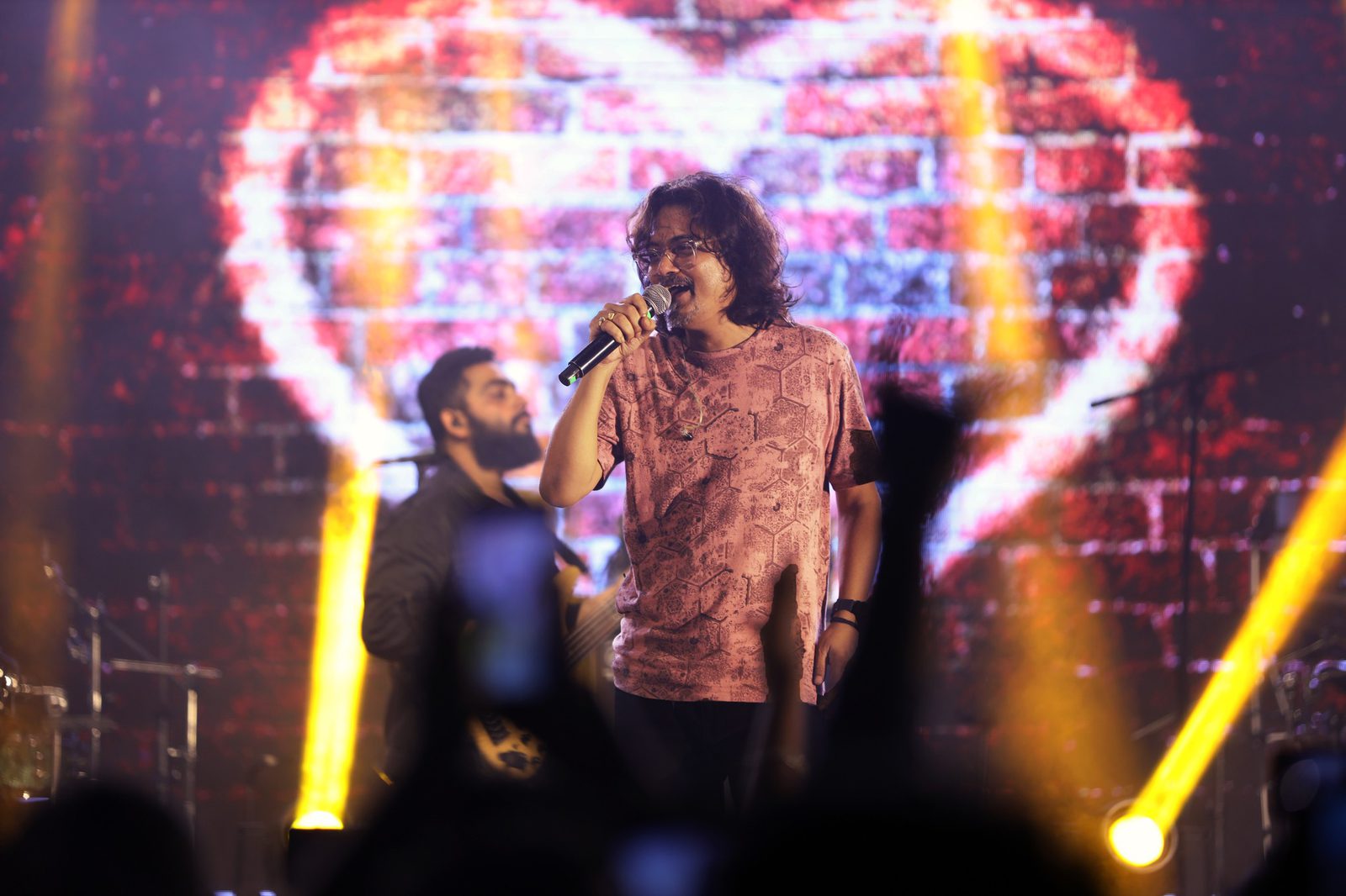 A singer at the mic with a huge illuminated heart filling the screen behind him