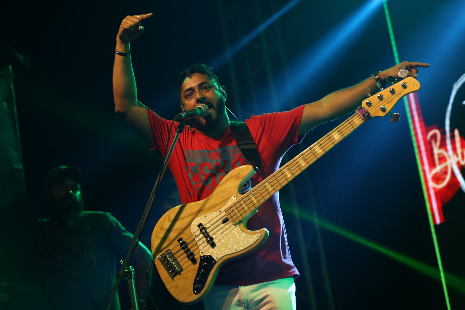 The bass player in a red t-shirt, both arms up, singing into the mic