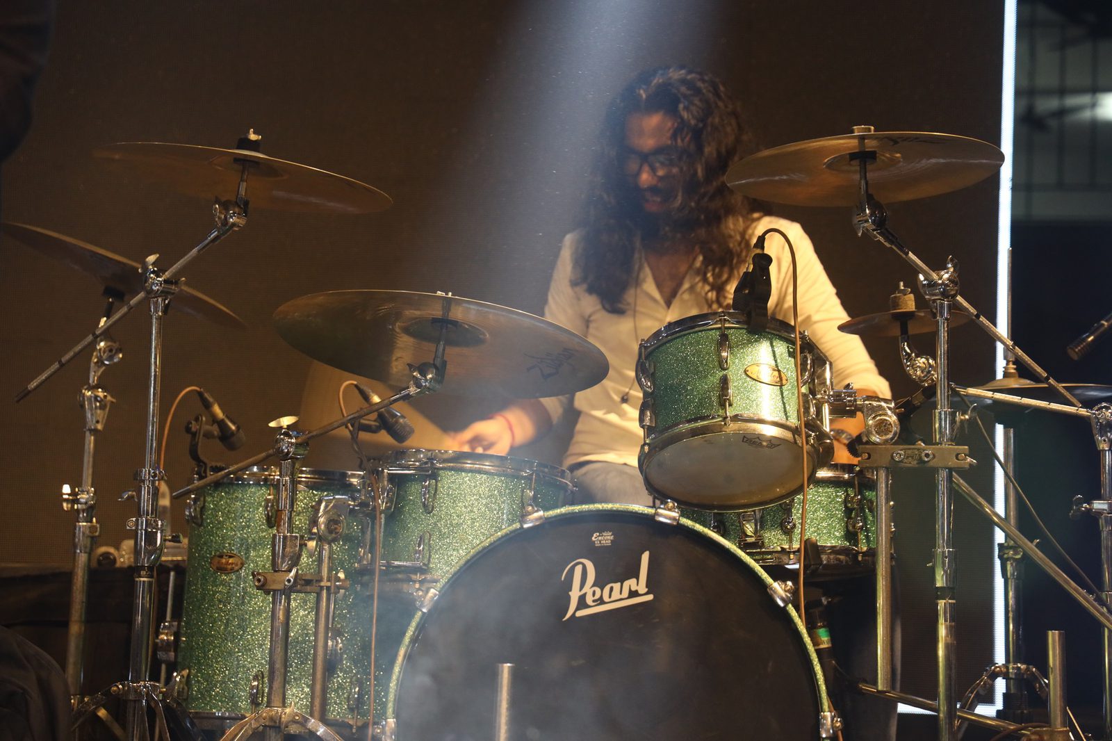 The drummer at a green sparkle kit, lit by one beam through the smoke