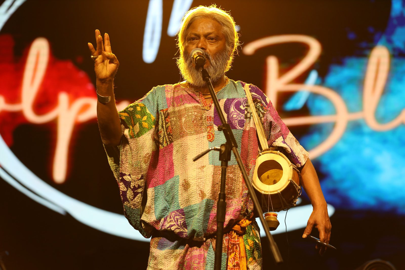 The same singer with a hand raised mid-phrase, The Bolpur Blues lettering glowing behind him