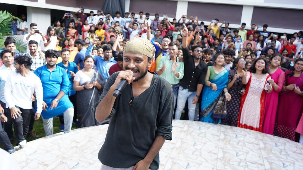 A singer on the courtyard dais with students crowded around him, phones up, cheering