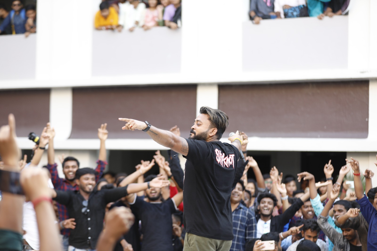 A singer with both arms flung out to a crowd of students, every hand in the air