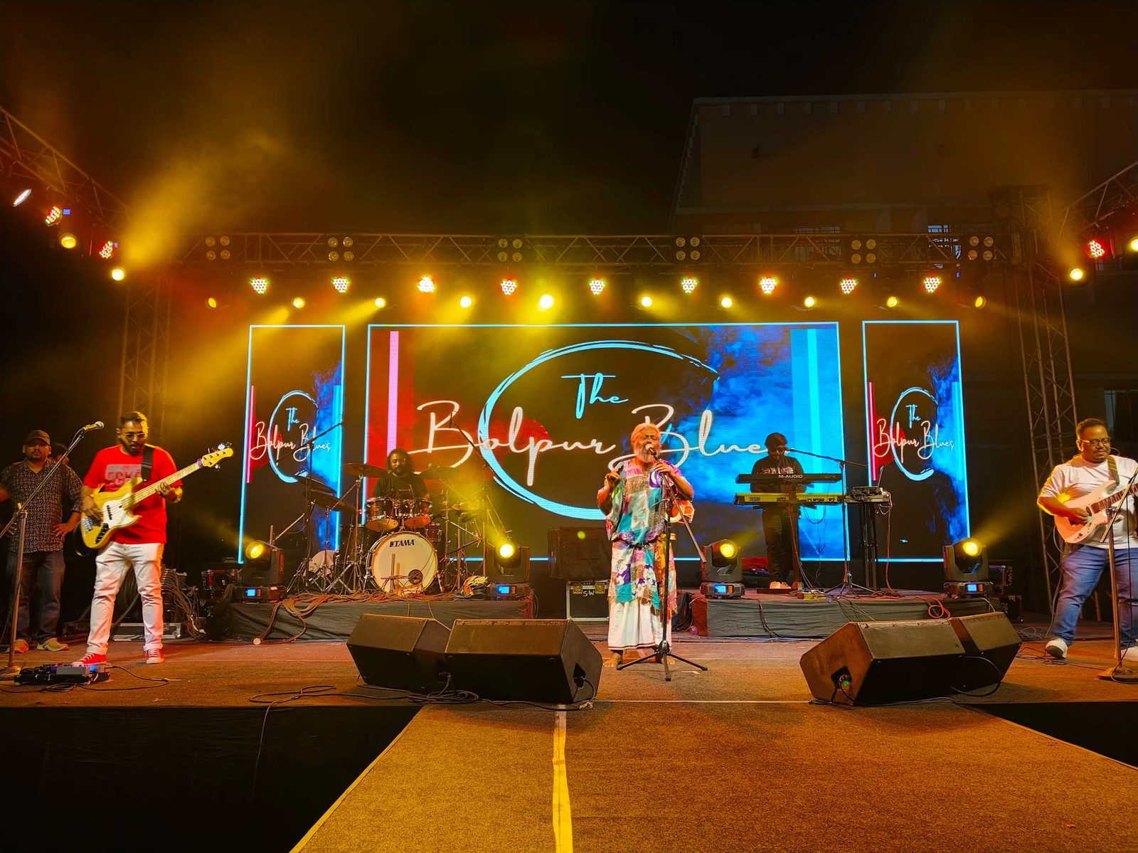 The Bolpur Blues across the stage, the band's name in neon script on the screen behind them
