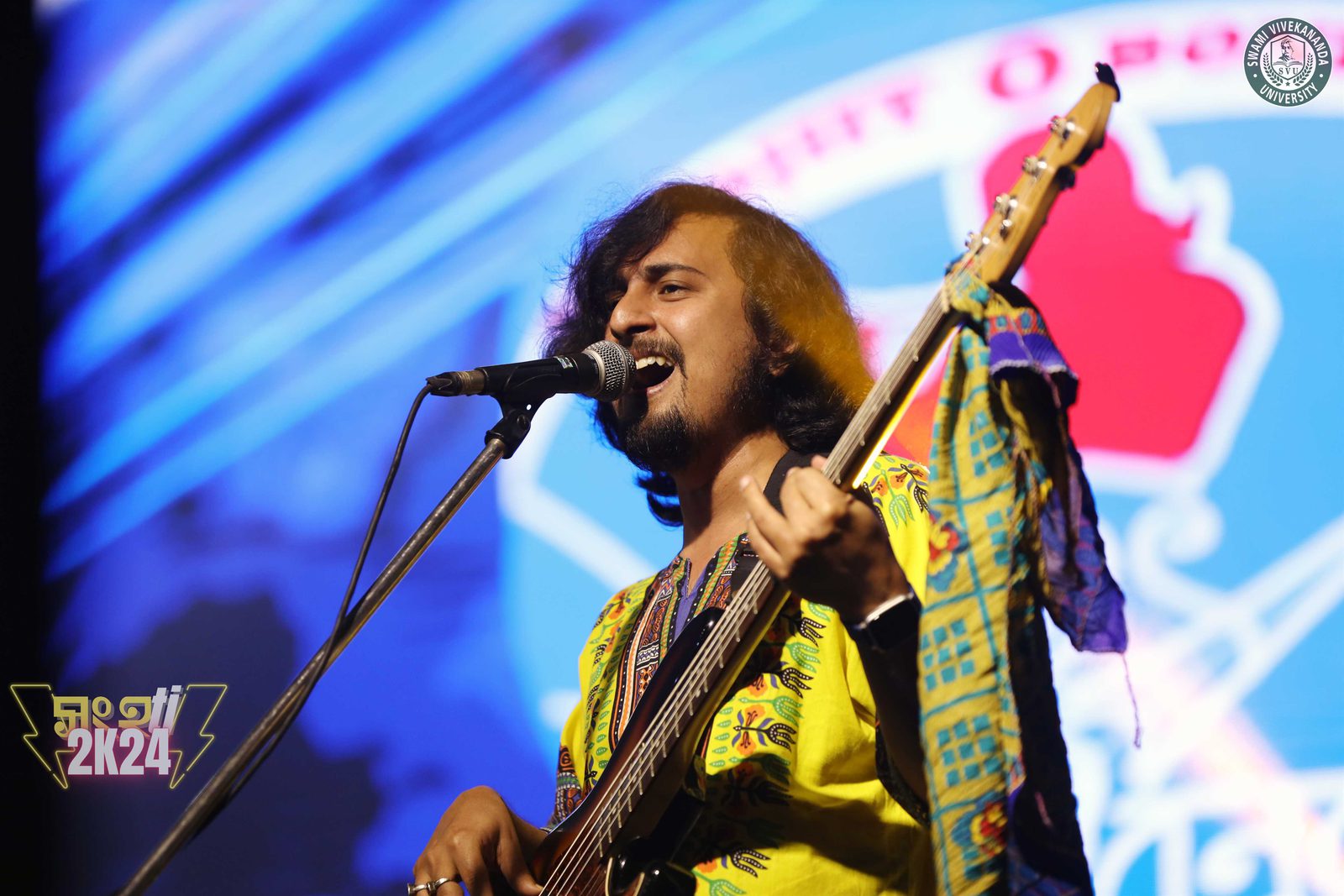 The bass player in a yellow printed kurta singing into the microphone