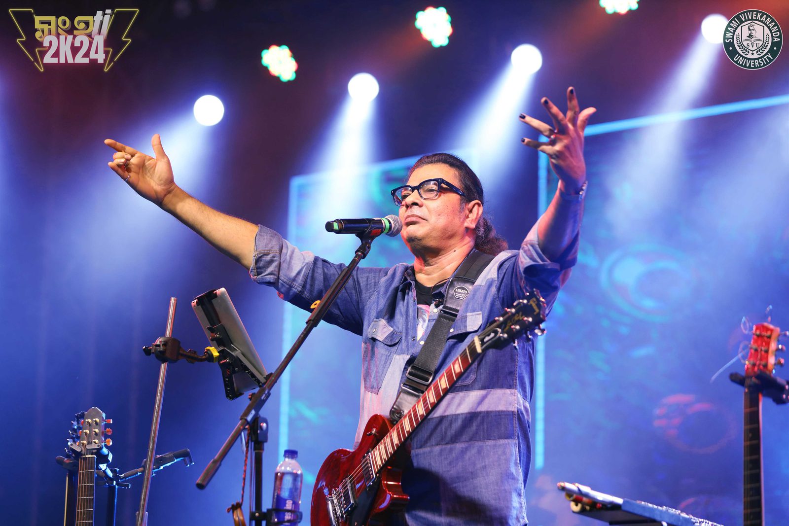 The frontman with both arms raised, calling the crowd in under blue stage light