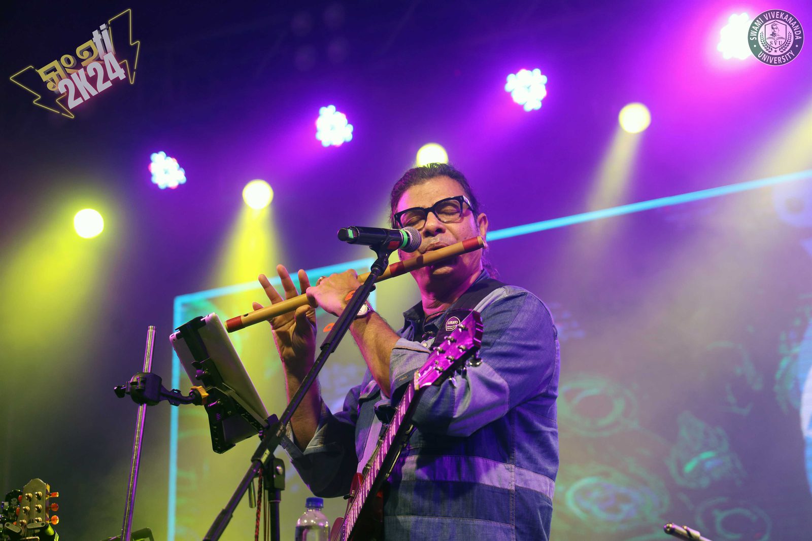 A bansuri solo at the microphone, the stage washed in purple and yellow