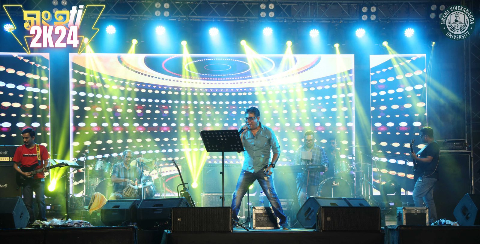 The whole band spread across the stage — guitars either side, tabla at the left, LED wall behind