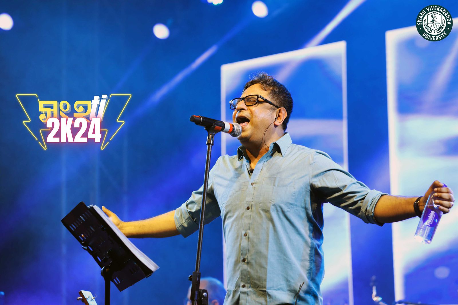 A singer with his arms thrown wide at the mic stand, music folder open in front of him